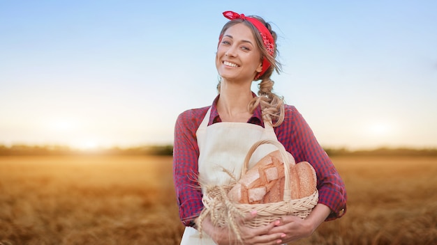 Coltivatore femminile in piedi campo agricolo di grano donna panettiere azienda cesto di vimini pane prodotto