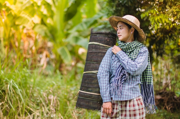 A female farmer with fish trap walks along her field.