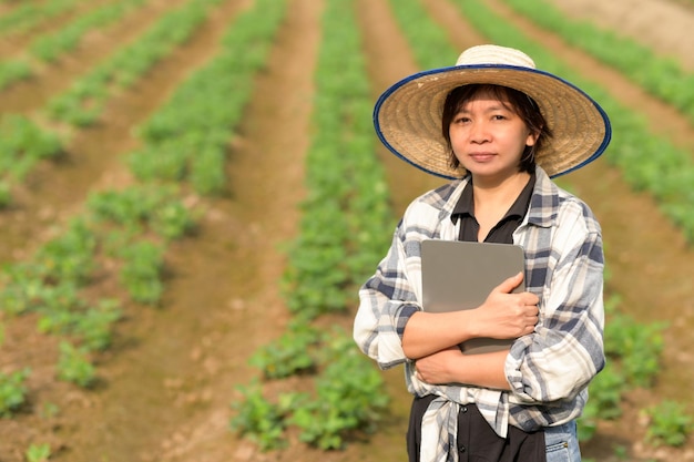 タブレットを持った女性農家が有機野菜畑に立つスマートファームスマート農家