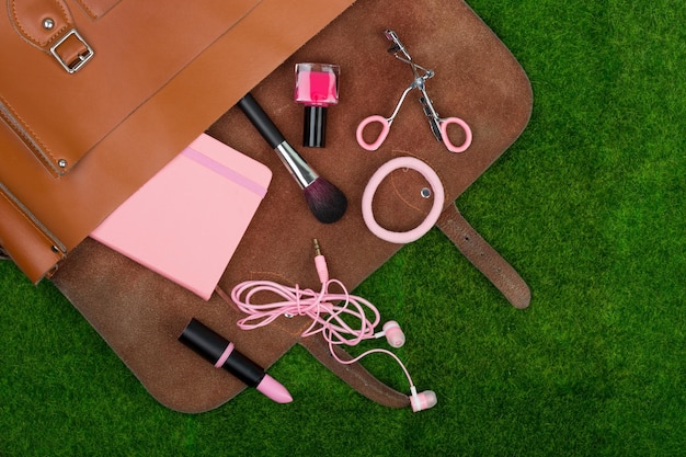 Female fashion accessories bag note pad headphones lipstick and other essentials on the grass