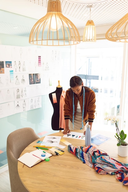 Female fashion designer looking at sketches on table in a modern office