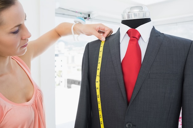 Female fashion designer measuring suit on dummy