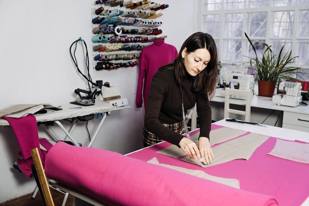 Женский модельер портной делает выкройки на рабочем месте в швейной мастерской Швея работает с выкройкой на столе в ателье