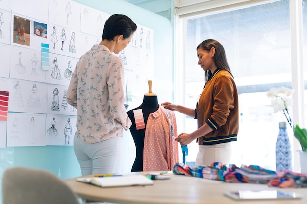 Female fashion designers working together working on garment on dressmaker model