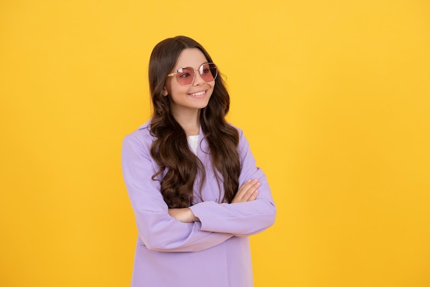 Female fashion model. pretty look of young girl in jacket. portrait of happy child on yellow background. express positive emotions. cheerful kid with curly hair in sunglasses. beauty and fashion.