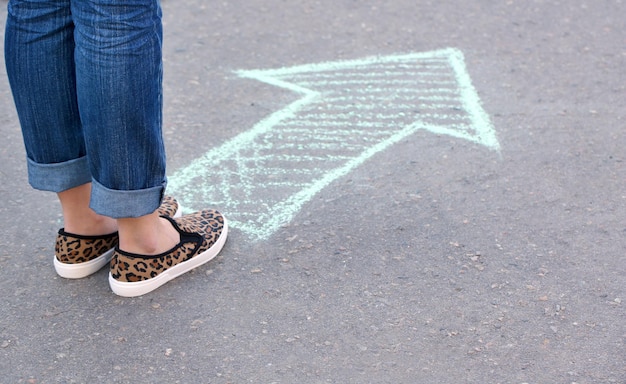 Female feet and drawing arrow on pavement background