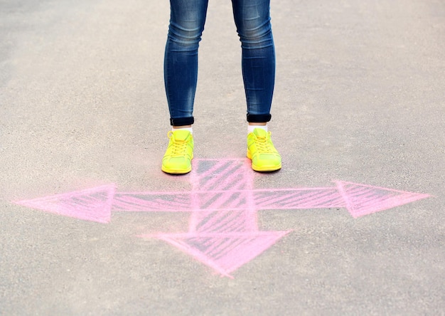 女性の足と舗装の背景に矢印を描く