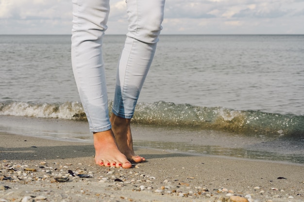 裸足のジーンズの女性の足はビーチで海の水の上を歩く