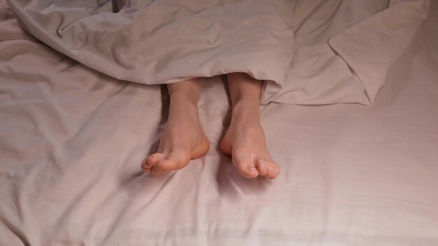 여자 발은 저녁에  시트 위에 있는 담요 에서 잠을 자면서 움직인다. 여자 소녀는 집 침실의 침대 위에서 벌거벗은 다리로 잠을 자고 있다.