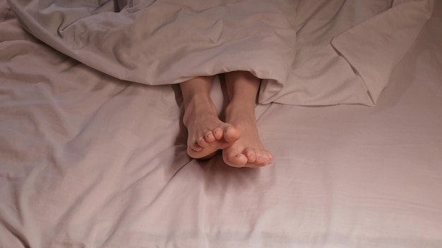 female feet move in their sleep at evening under a blanket on a white sheet A woman girl sleeps on a bed in a home bedroom with bare legs foot