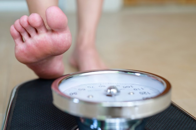 Female feet standing on electronic scales for weight control on wooden background. The concept of slimming and weight loss