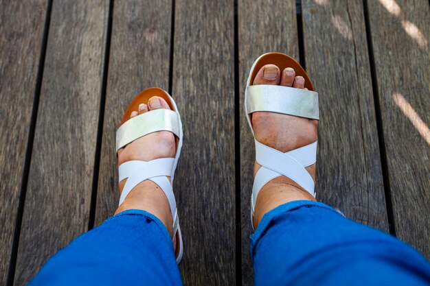 Female feet in white sandals on the wooden floor.