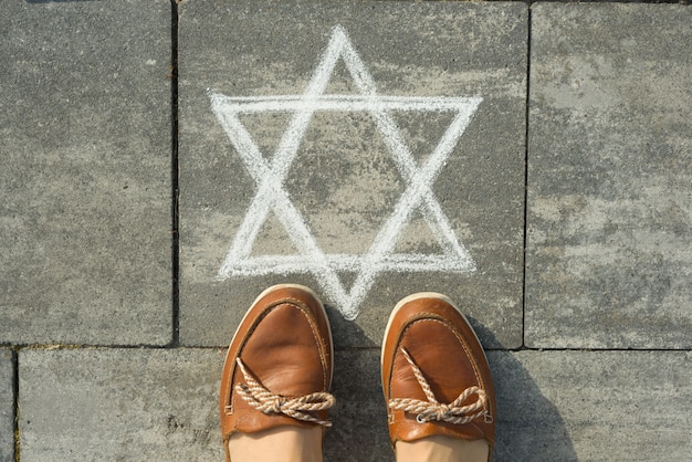 Female feet with abstract image of six pointed star, written on grey sidewalk