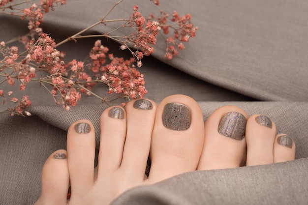 Female feet with beige nail design on gray fabric surface.