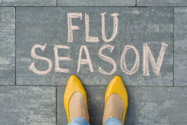 Female feet with text flu season written on grey sidewalk