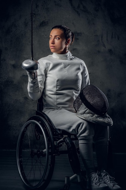 Female fencer in wheelchair with safety mask of a face holding rapier, dust effect on image.