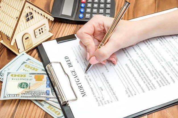 Female filling mortgage deed on the table with model of house money and calculator