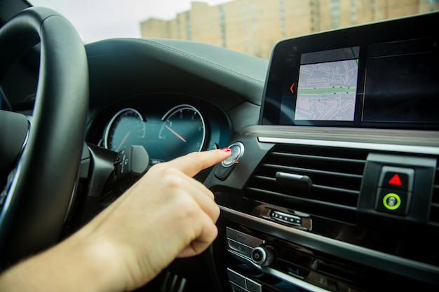 Female finger presses the start stop engine button on car dashboard closeup car interior details