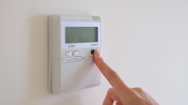 Female finger pressing air conditioner button on wall closeup