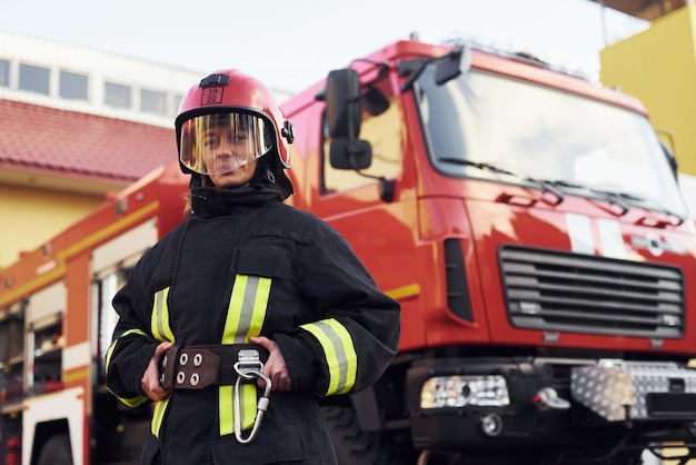 Female firefighter in protective uniform standing near\
truck