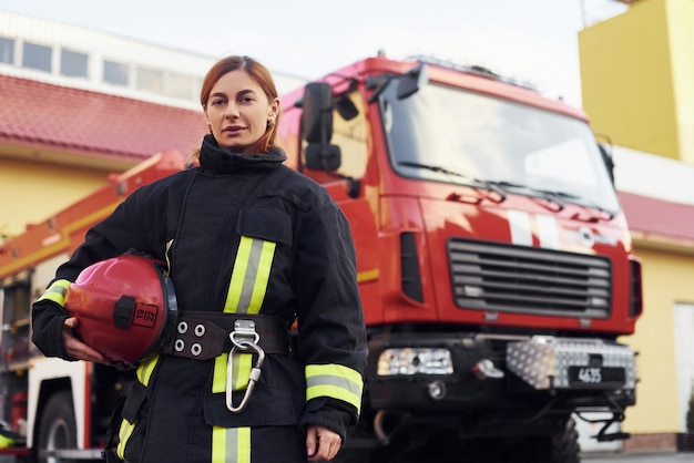 Female firefighter in protective uniform standing near truck