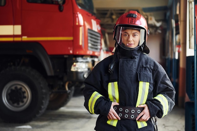 Female firefighter in protective uniform standing near truck