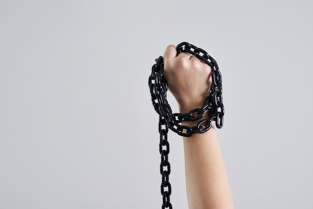 Female fist holding metal chain high up over grey wall