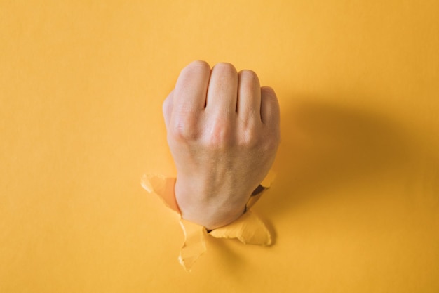 Female fist punching through a paper, isolated on a yellow background.