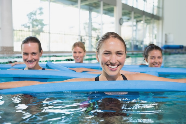 Female fitness class doing aqua aerobics with foam rollers