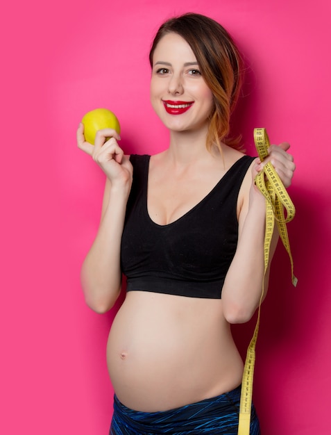  female in fitness clothes with tape measure and apple