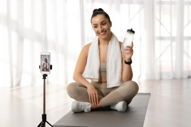 Photo female fitness instructor recommending water drinking broadcasting from home