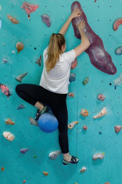 Женская фитнес-профессиональная альпинистка тренируется в бульдерном тренажерном зале Мышечная женщина с спортивным телом, одетая в черное, скалится на искусственной красочной скальной стене Активный образ жизни и концепция бульдера