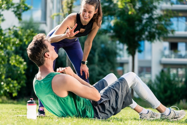 Female fitness trainer motivating man doing crunches