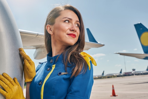 female flight attendant in leather gloves leaning on the aircraft fuselage