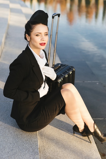 A female flight attendant in uniform sits on the steps next to the suitcase