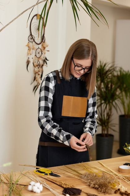 木製のテーブルでドライフラワーとハーブの組成物を作る女性の花屋花屋