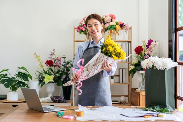 写真 黄色の菊の花束を持ったエプロンの女性花屋