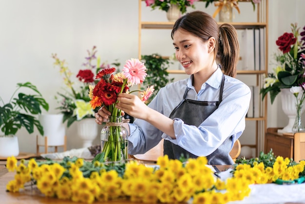 写真 エプロンを着た女性花屋が笑顔でガーベラの花を生ける