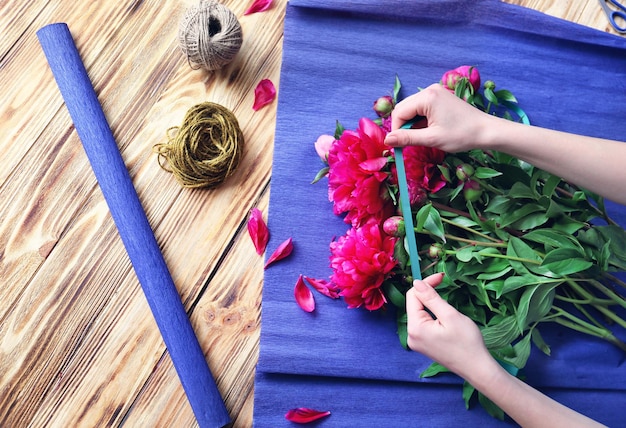 Female florist making bouquet of beautiful peonies in flower shop closeup