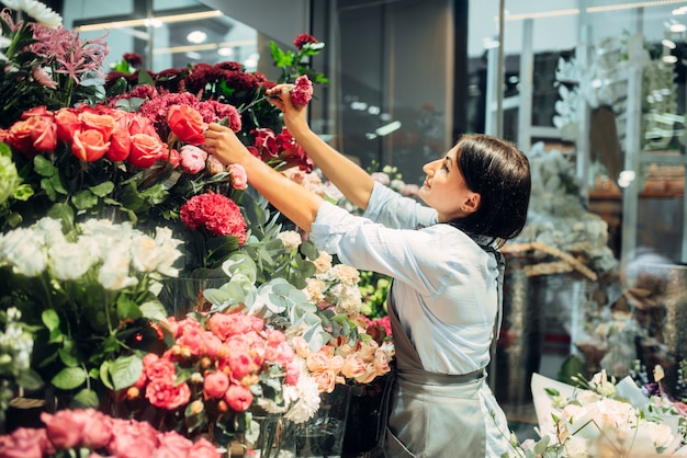 花屋では、女性の花屋が花束を作るために花を選びます。