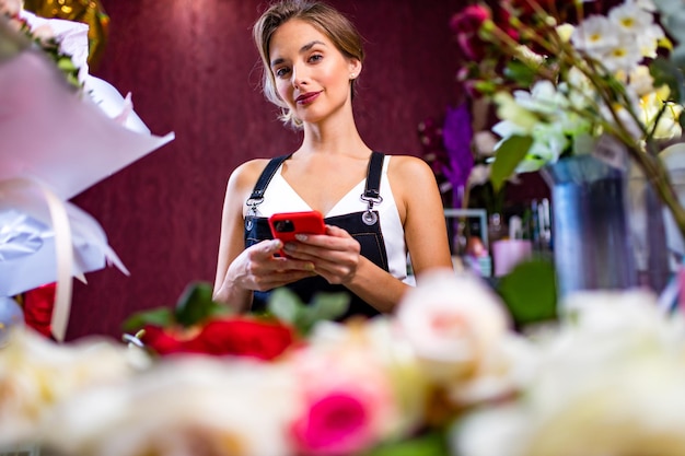 Female florist standing at her flower shop counter using mobile phone delivery