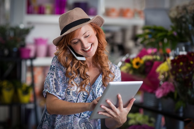 Fiorista femminile che parla sul telefono cellulare mentre per mezzo della compressa digitale