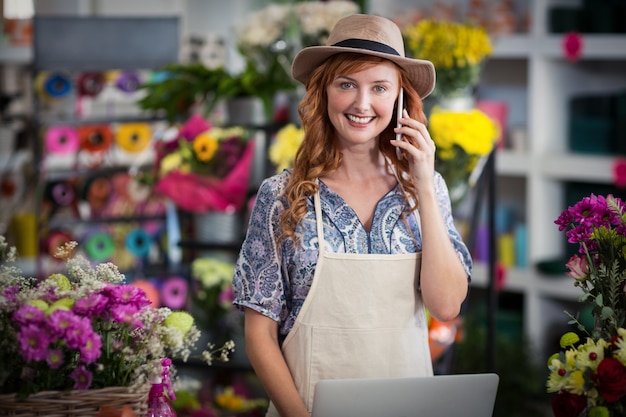 Female florist talking on mobile phone while using laptop