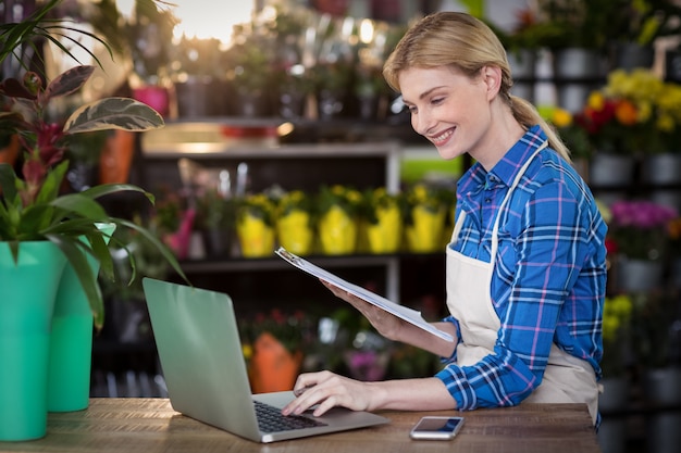 Female florist using laptop while holding clipboard