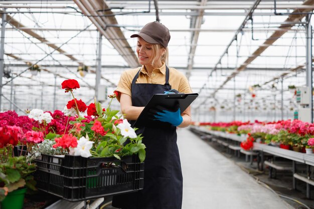 クリップボードを持つ女性の花屋は温室内の農産物を追跡します