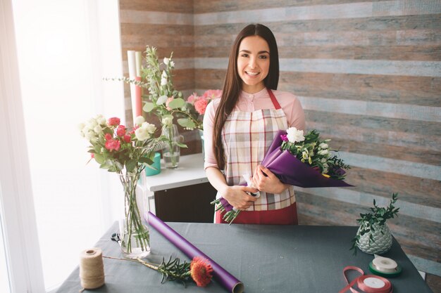 Female florist at work: pretty young dark-haired woman making fashion modern bouquet of different flowers. Women working with flowers in workshop