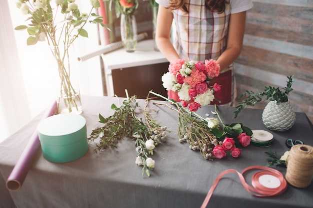 Female florist at work: pretty young dark-haired woman making fashion modern bouquet of different flowers. Women working with flowers in workshop