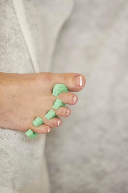 뷰티 살롱에서 밝은 배경 페디큐어에 녹색 색상의 발가락 구분 기호가 있는 여성 발