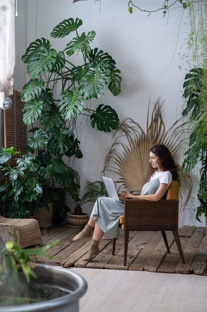 도시 정글 내부 또는 집 정원에서 온라인으로 일하는 여성 프리랜서 식물학 전문가