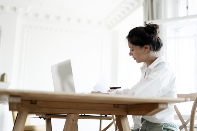 A female freelance designer works at home uses a laptop makes a\
report workplace in the office